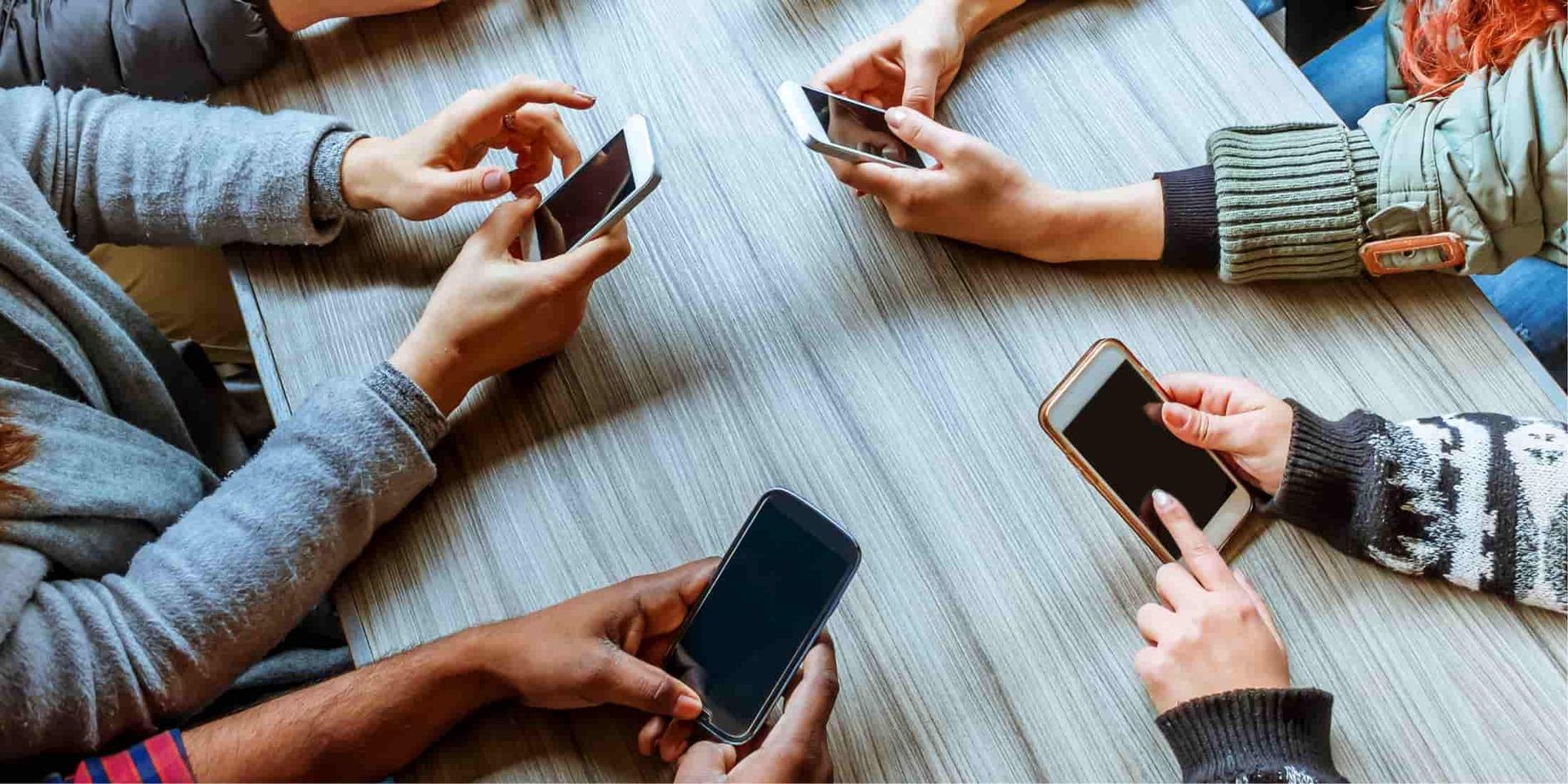 Group of people seated around a table, using smartphones.